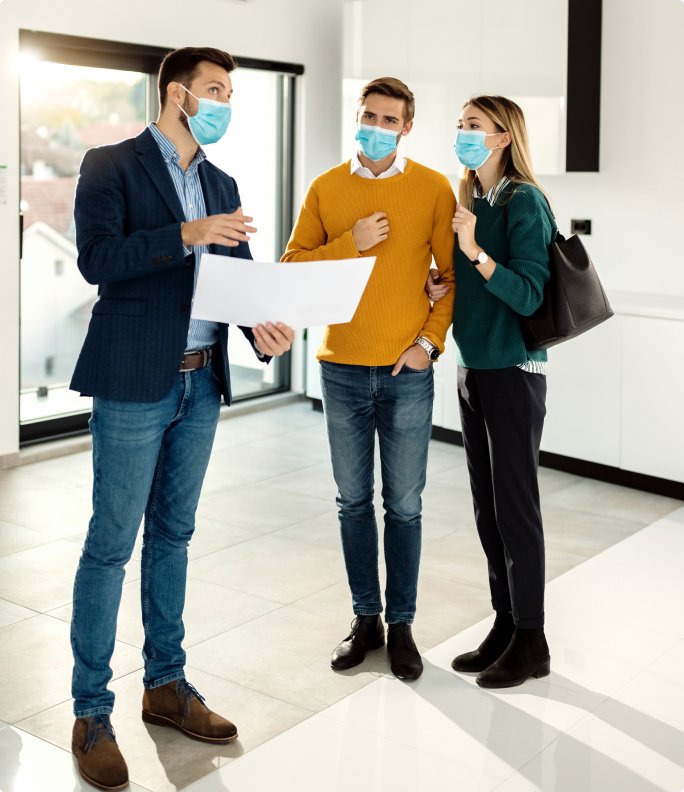 young-couple-buying-new-home-examining-blueprints-with-real-estate-agent-while-wearing-face-masks 1 (2)