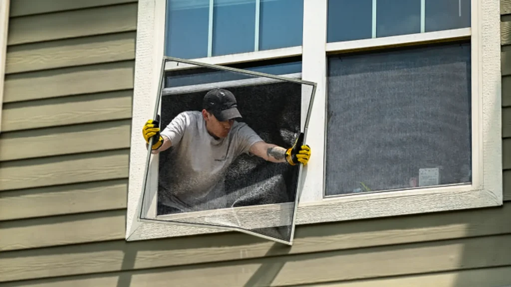 Temporary maintenance worker installing a window screen on a multifamily building